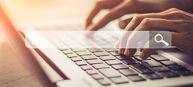 Two hands typing a search request on a laptop